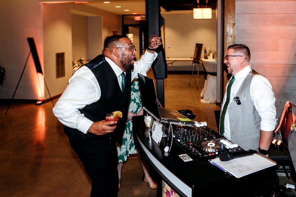 Travis laughing and hyping the crowd beside the DJ booth at a wedding